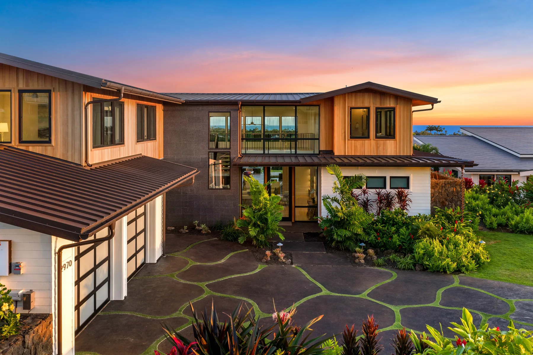A modern house with a paved courtyard and garden at sunset.