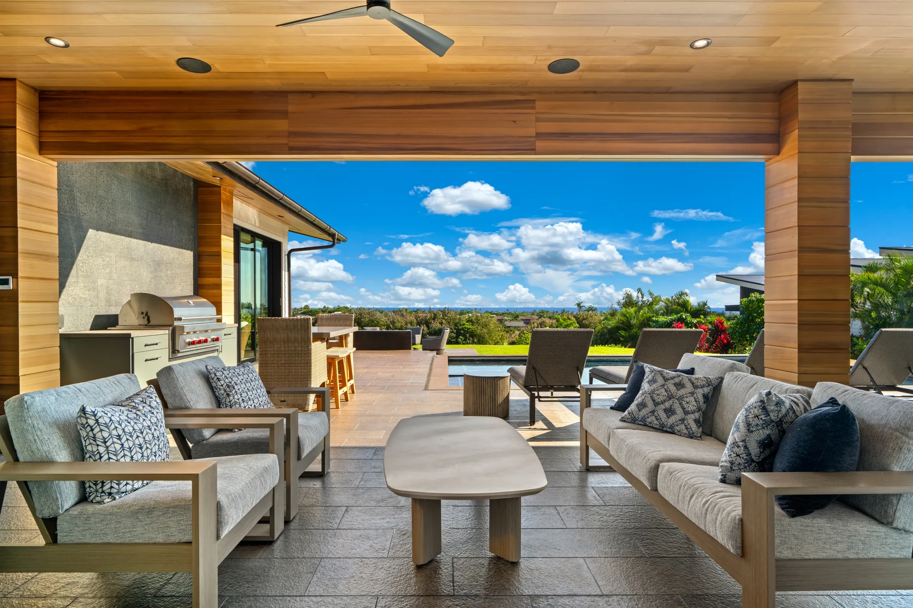 A covered outdoor lounge opens onto a terrace with seating and a clear view of the sky.