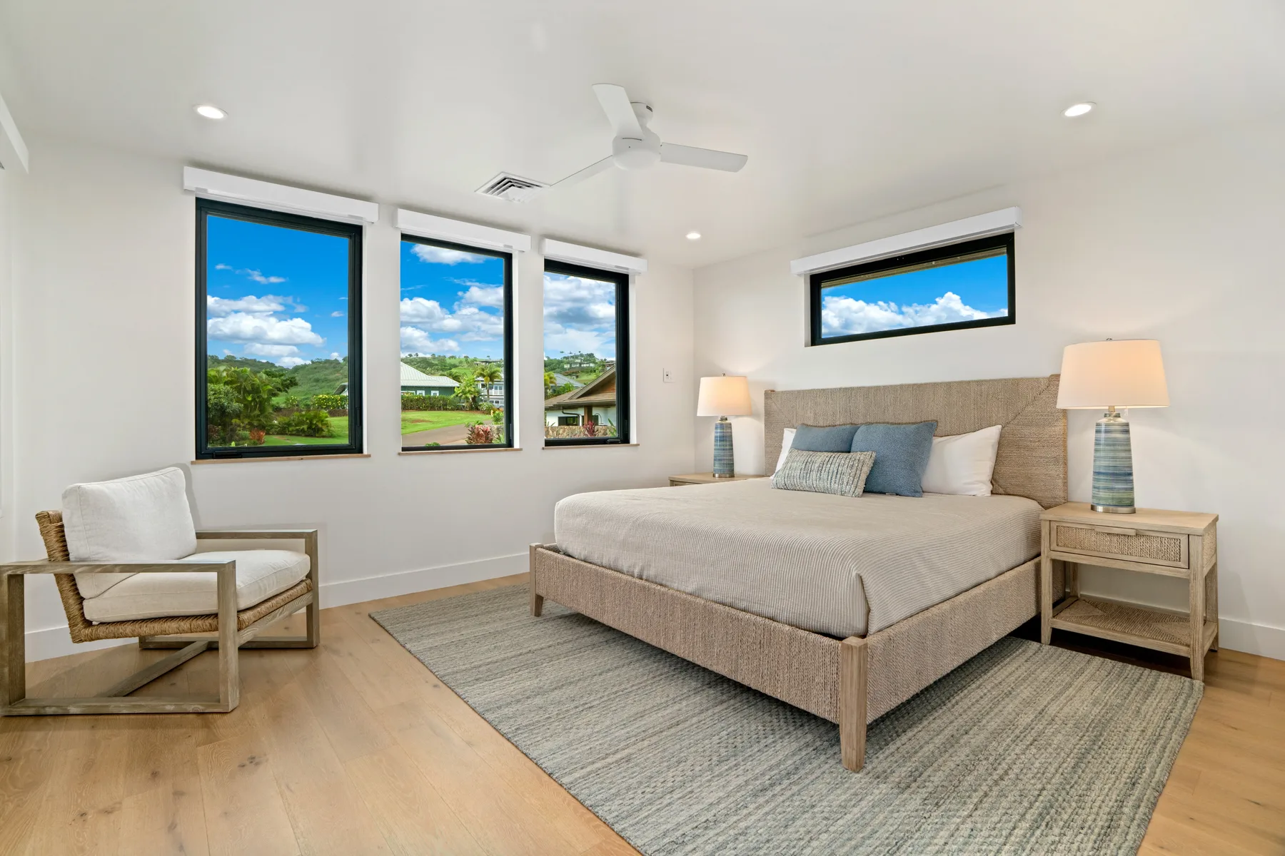 A bright bedroom with a large bed, bedside tables, and wide windows.