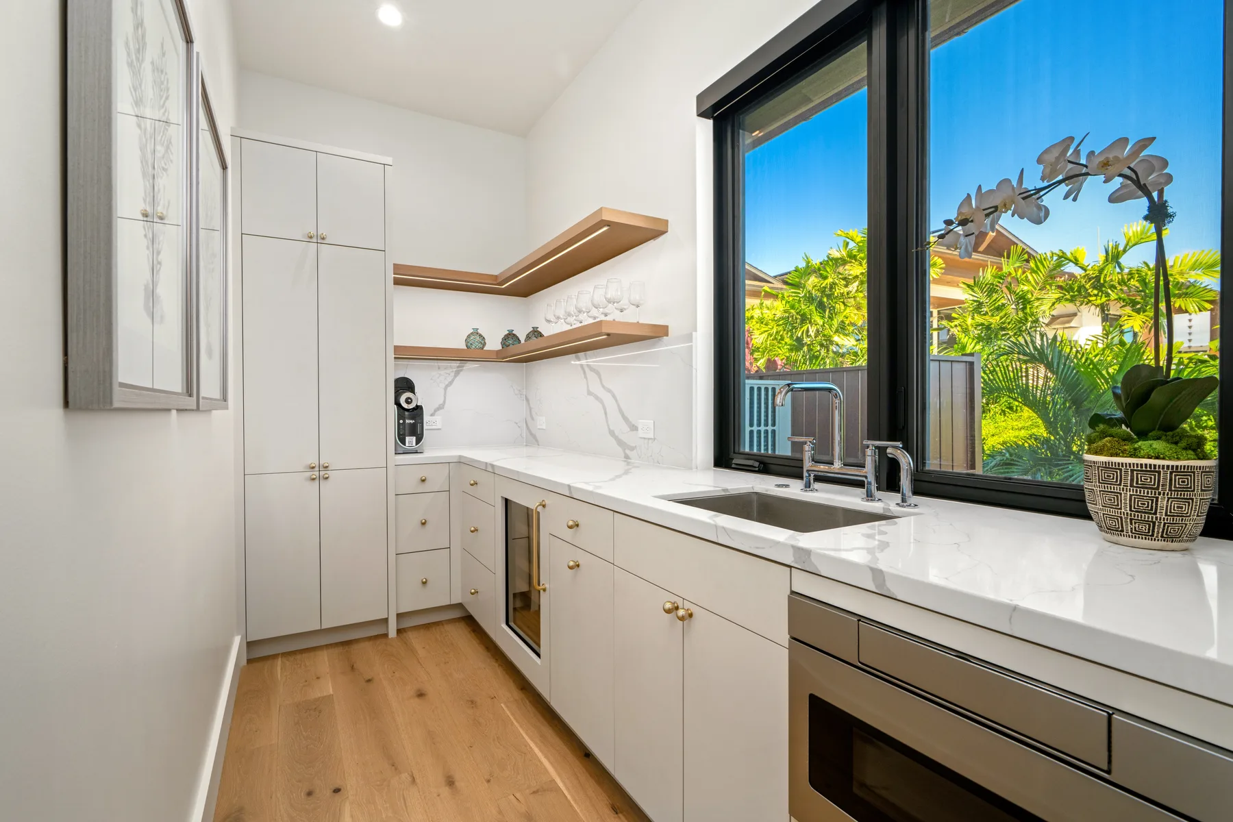 A bright kitchen with white cabinetry and a large window overlooking greenery.