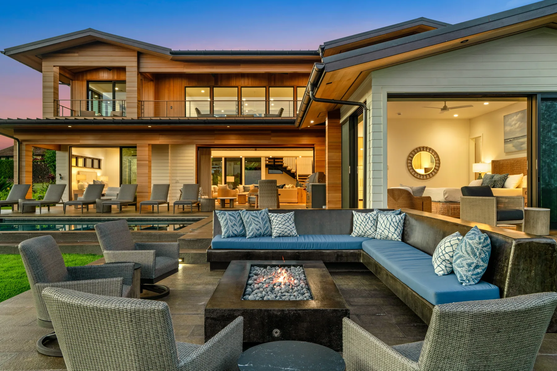A modern house opens onto an outdoor lounge with seating around a fire pit.