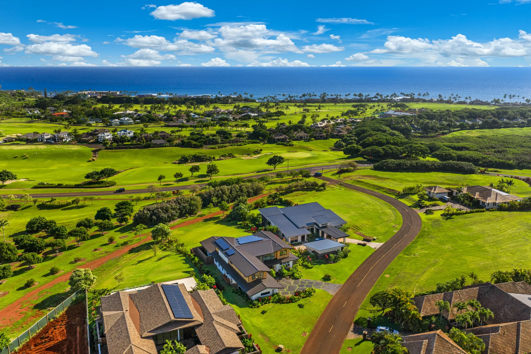 Aerial view of homes along a curving road, with green fields and the ocean beyond.