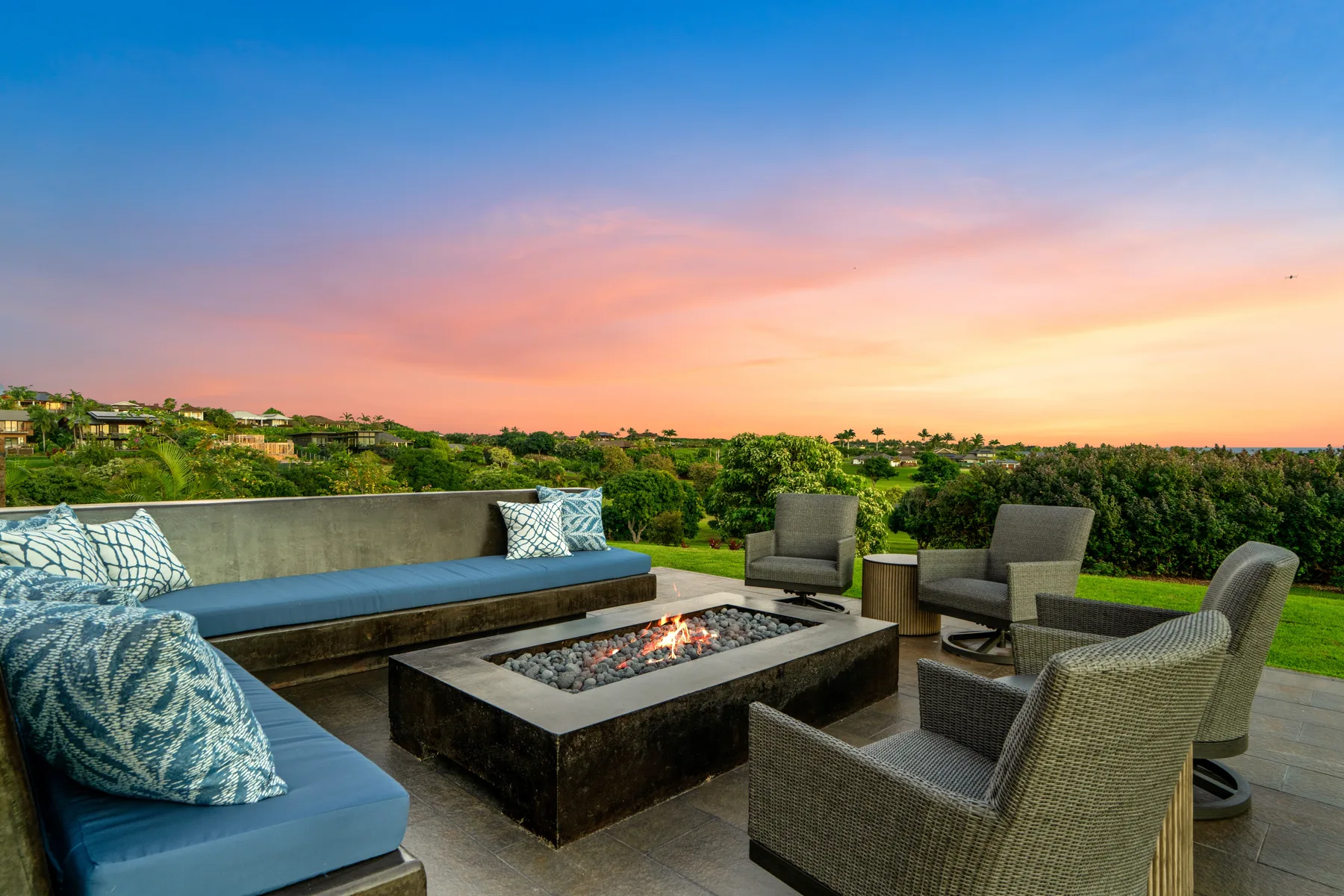 An outdoor patio seating area surrounds a rectangular fire pit at sunset.