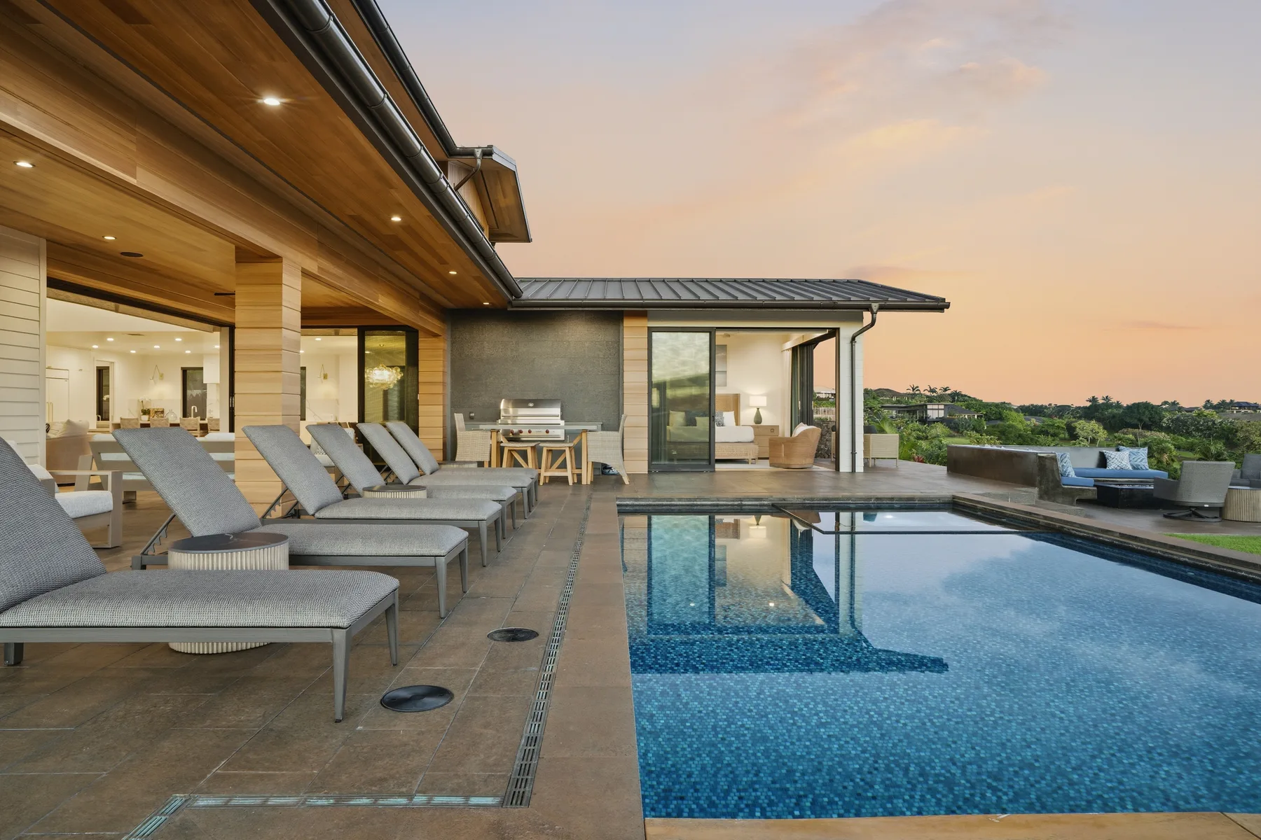 An outdoor pool beside a covered patio with lounge seating and a distant hillside view.