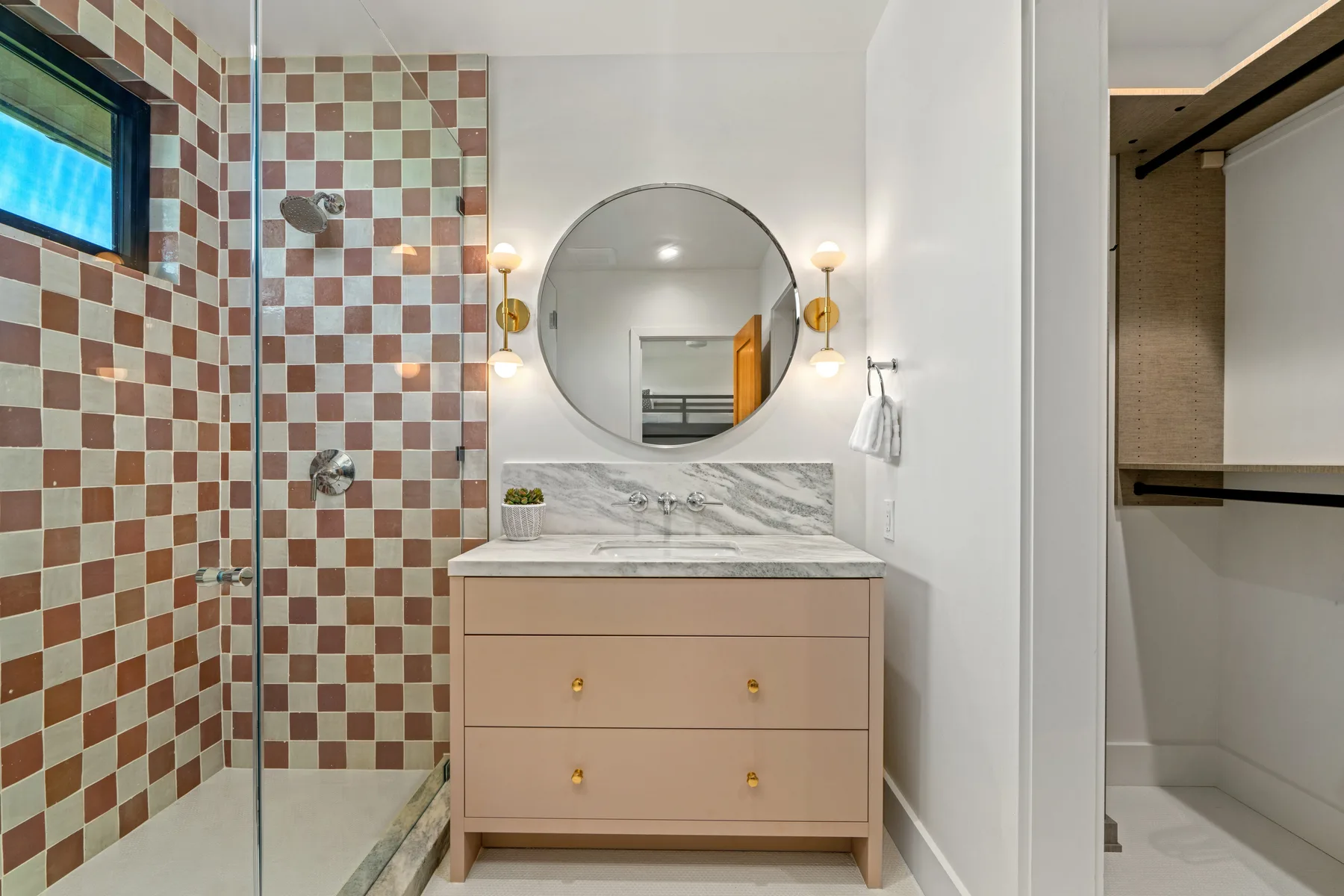 A bathroom vanity with a round mirror stands beside a tiled shower.