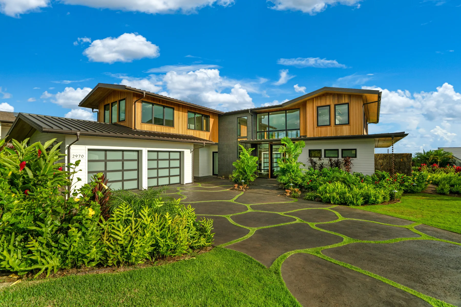 A modern house with large windows sits beside a curved paved driveway and landscaped greenery.