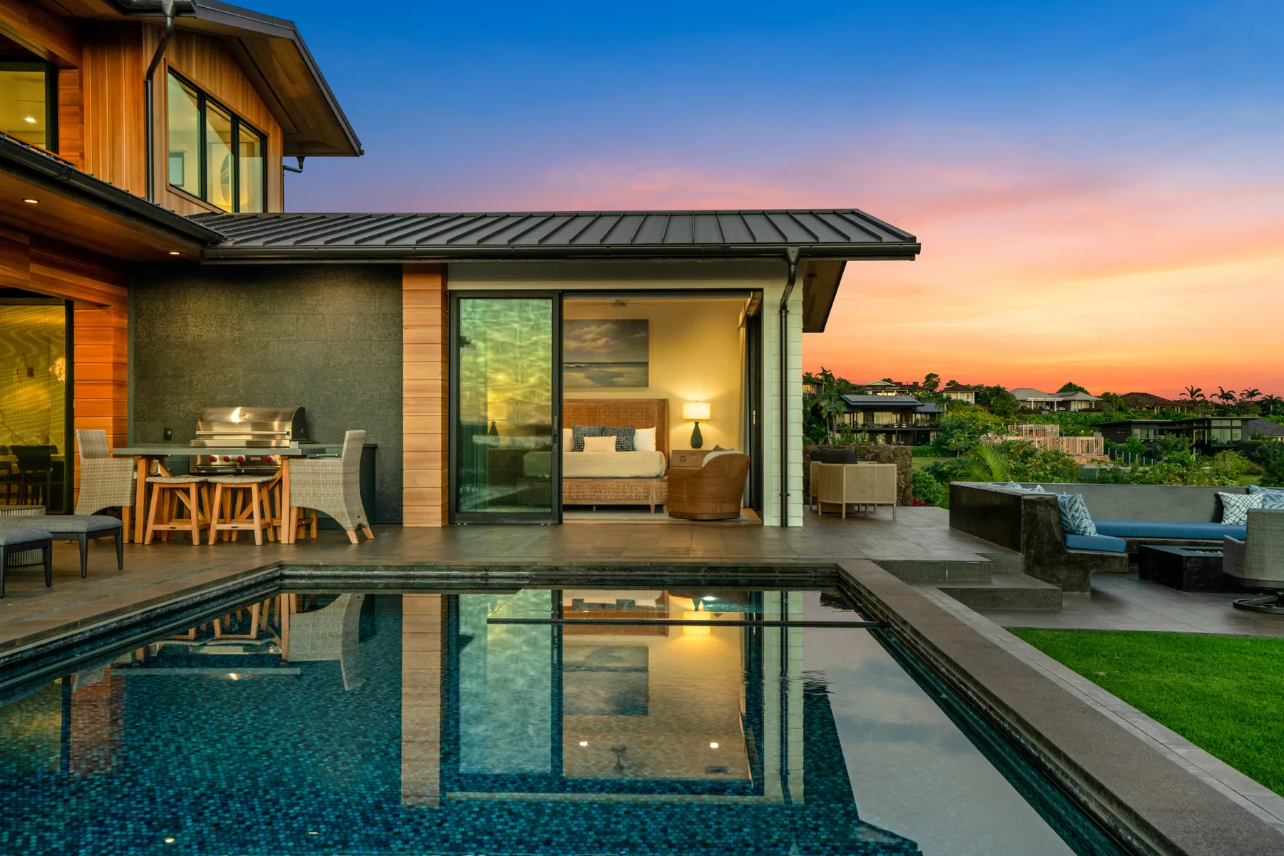A modern home opens onto a swimming pool, with an outdoor dining area at sunset.