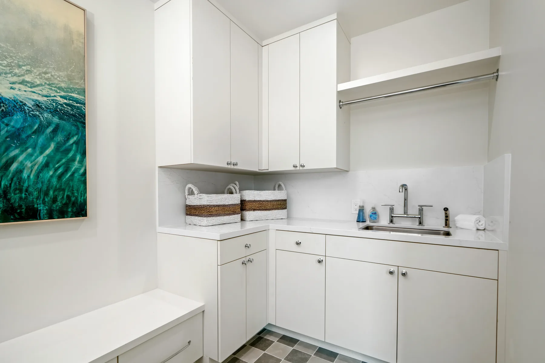 A bright laundry room with white cabinets, a sink, and a hanging rod.
