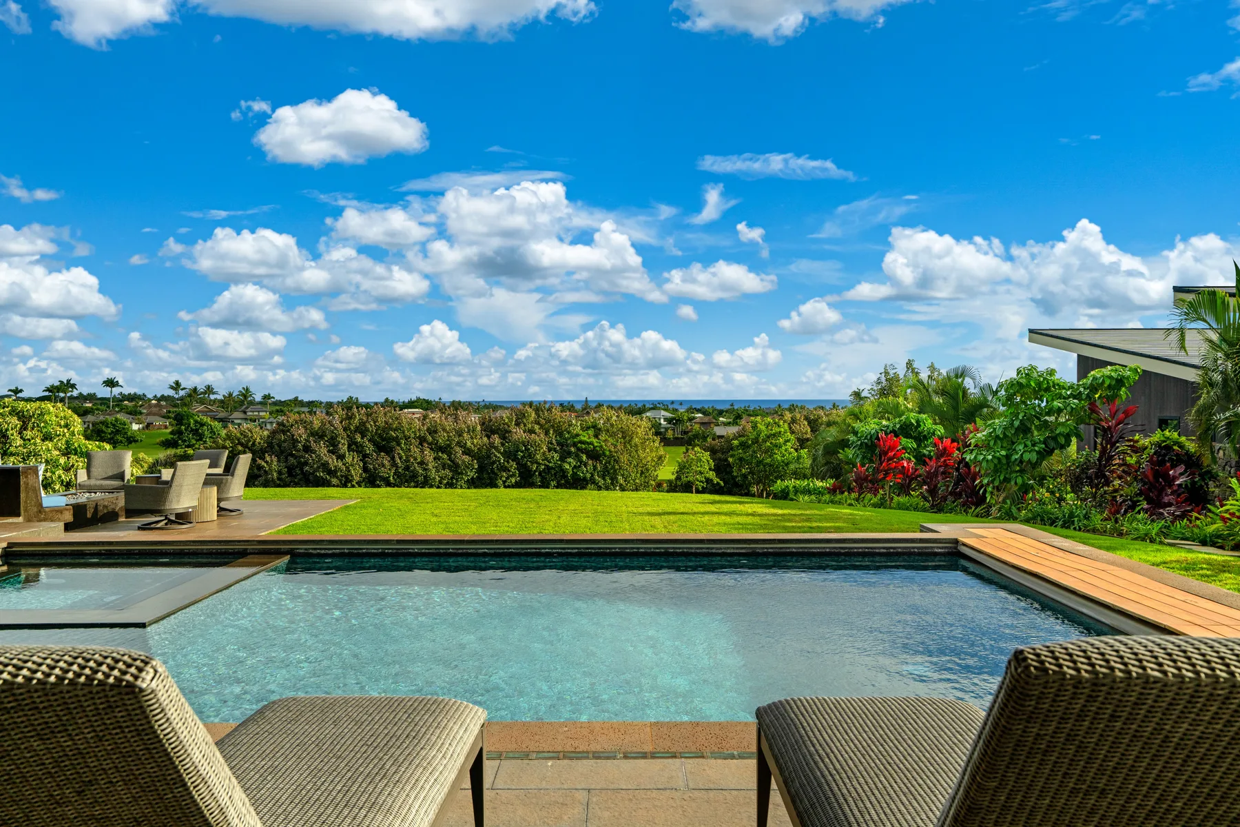 An outdoor swimming pool overlooks a green garden beneath a partly cloudy sky.