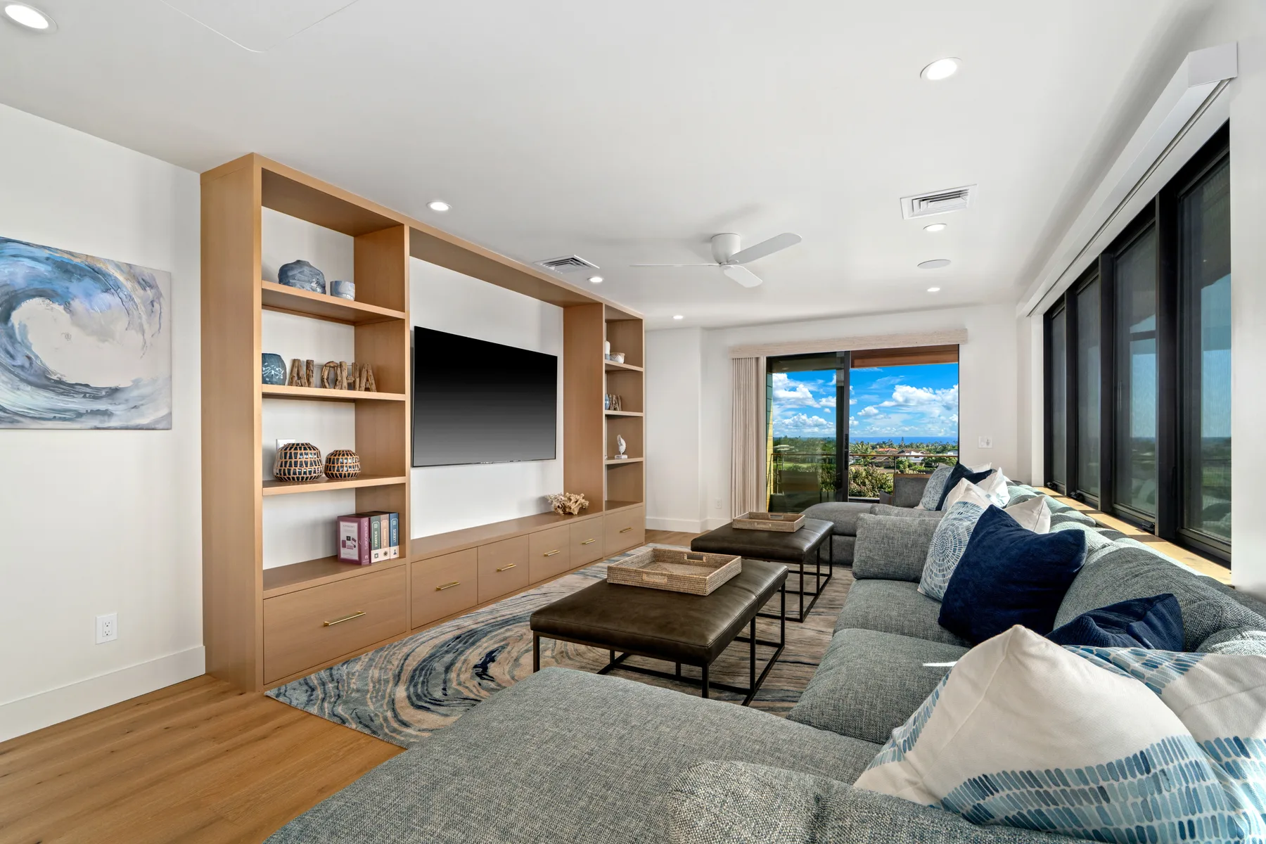 A bright living room with a large television and seating beside expansive windows.