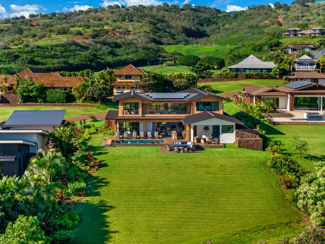 A modern house stands beside a broad green lawn on a lush hillside.