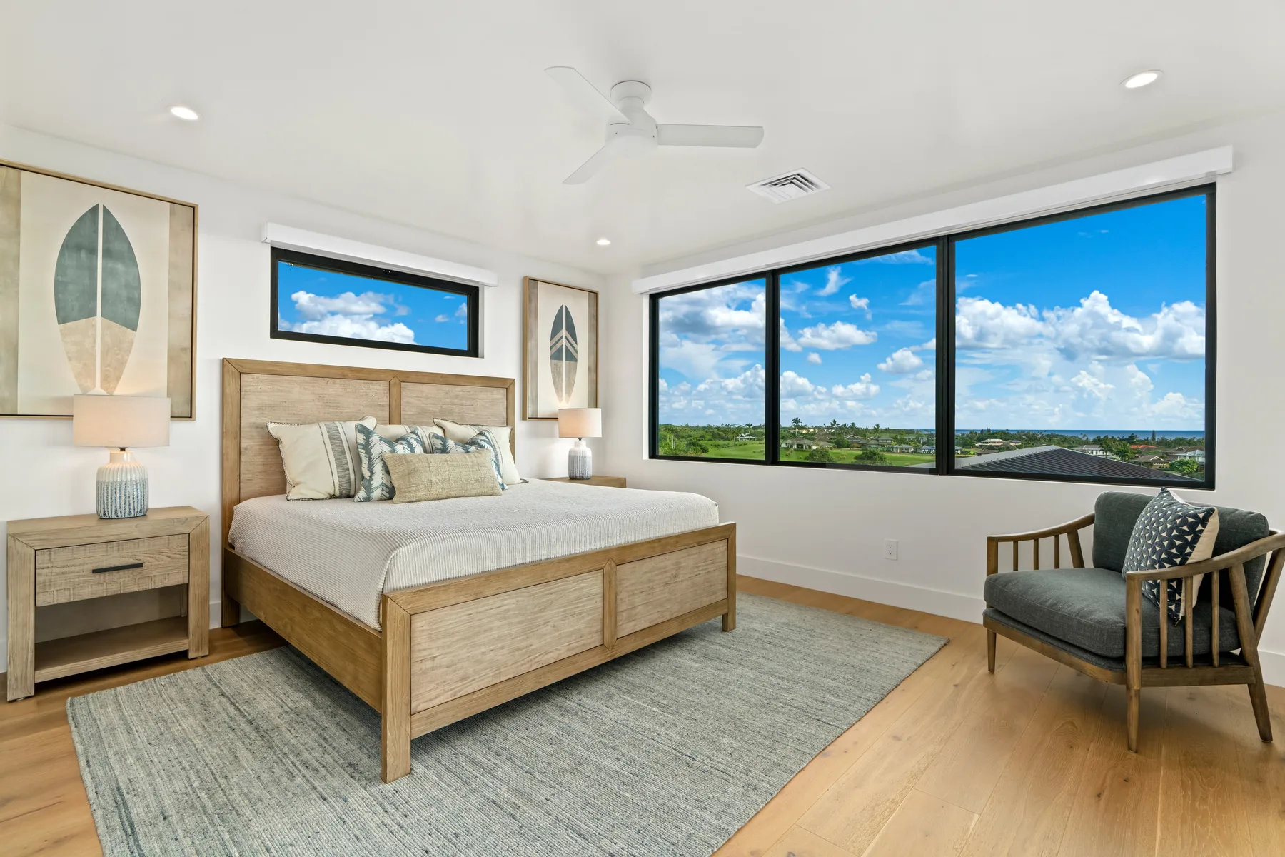 A bright bedroom with a bed beside large windows overlooking a green landscape.