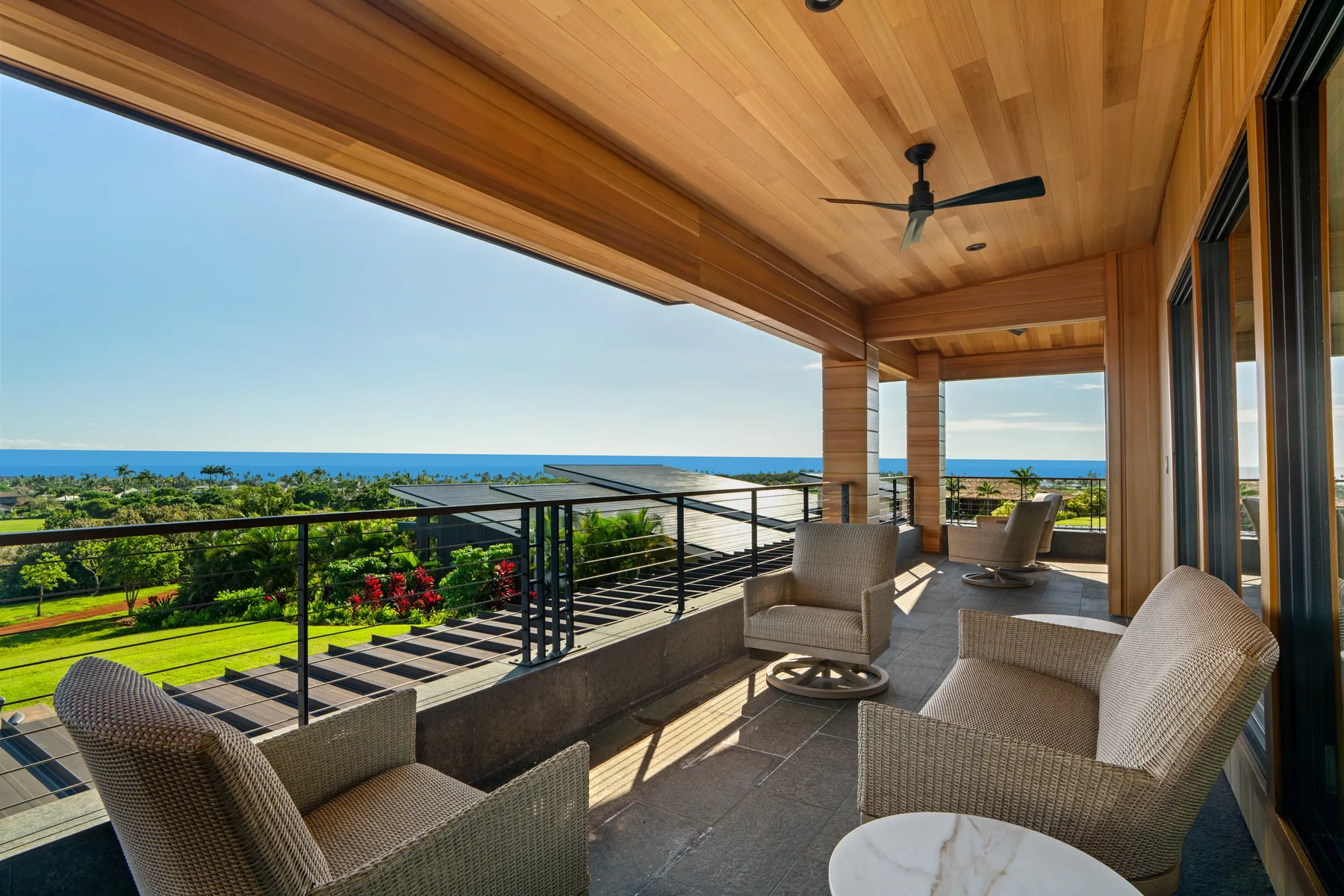 A covered terrace with woven seating overlooks gardens and the ocean.