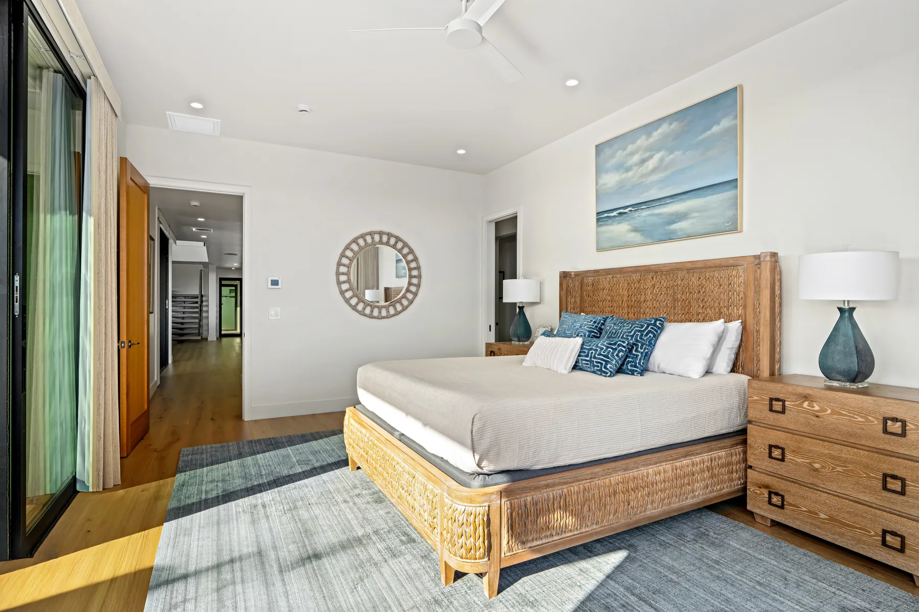 A bright bedroom with a large bed, bedside tables, and a framed beach painting.