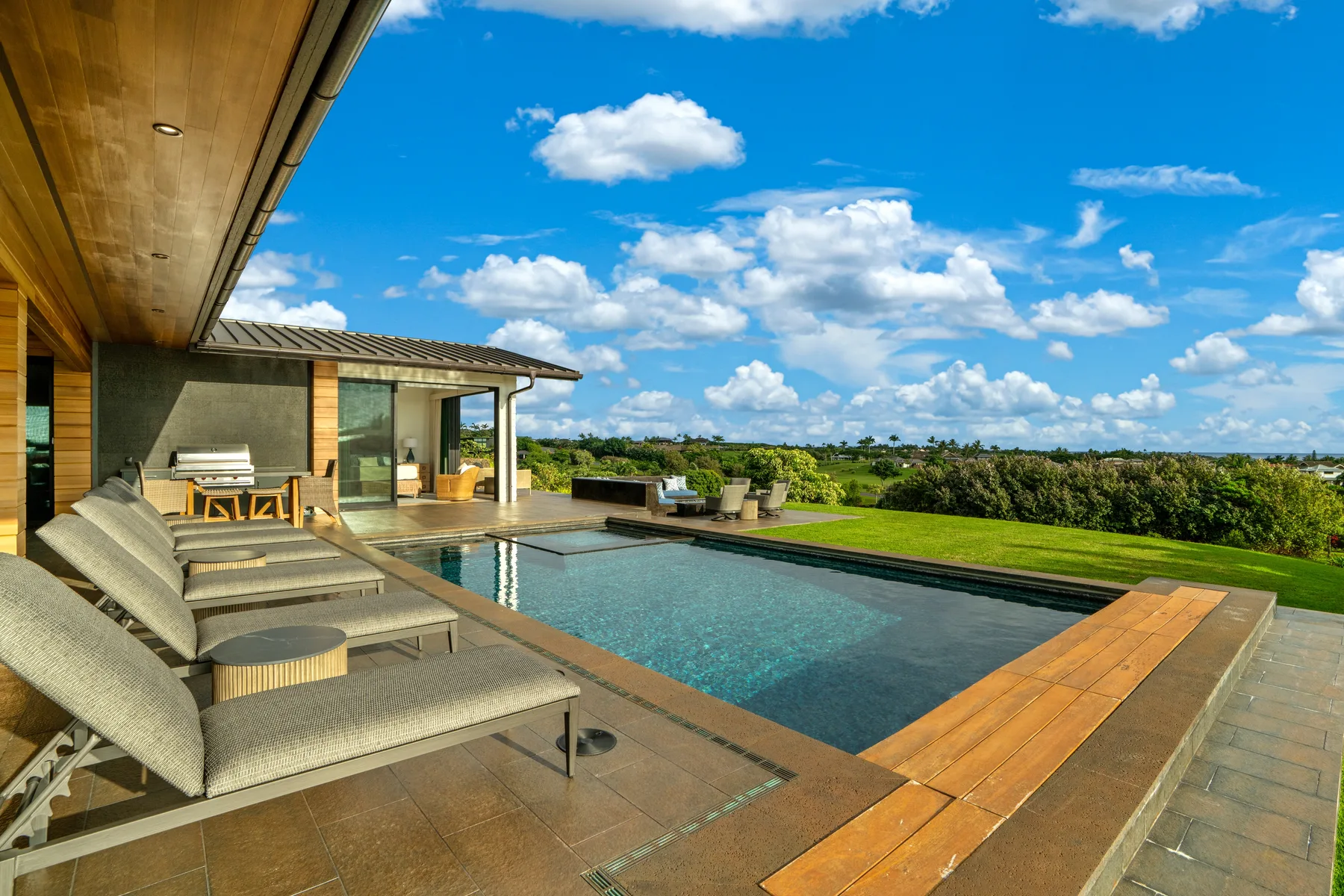 A modern house opens onto a swimming pool and outdoor seating area.