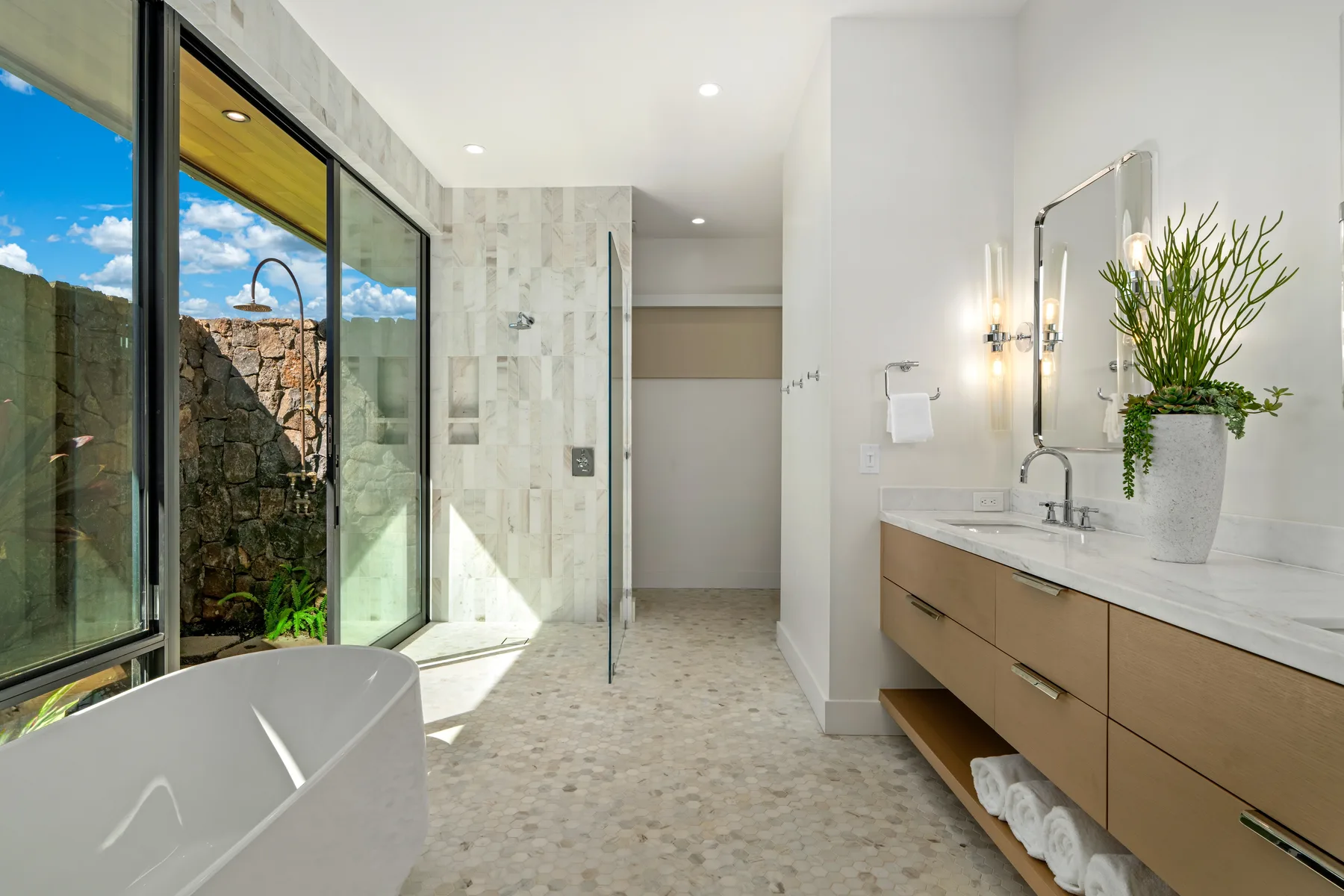 A bright bathroom with a bathtub, glass shower, and long vanity.