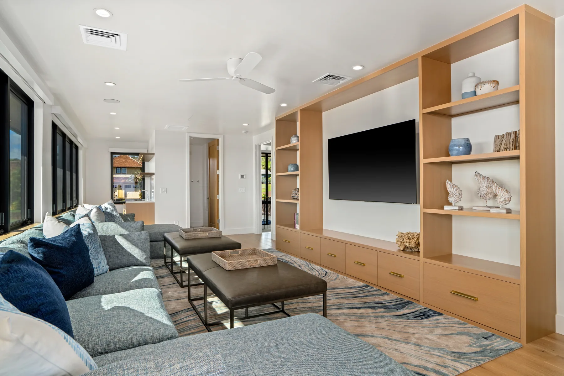 A bright living room has built-in wooden shelving around a wall-mounted television.