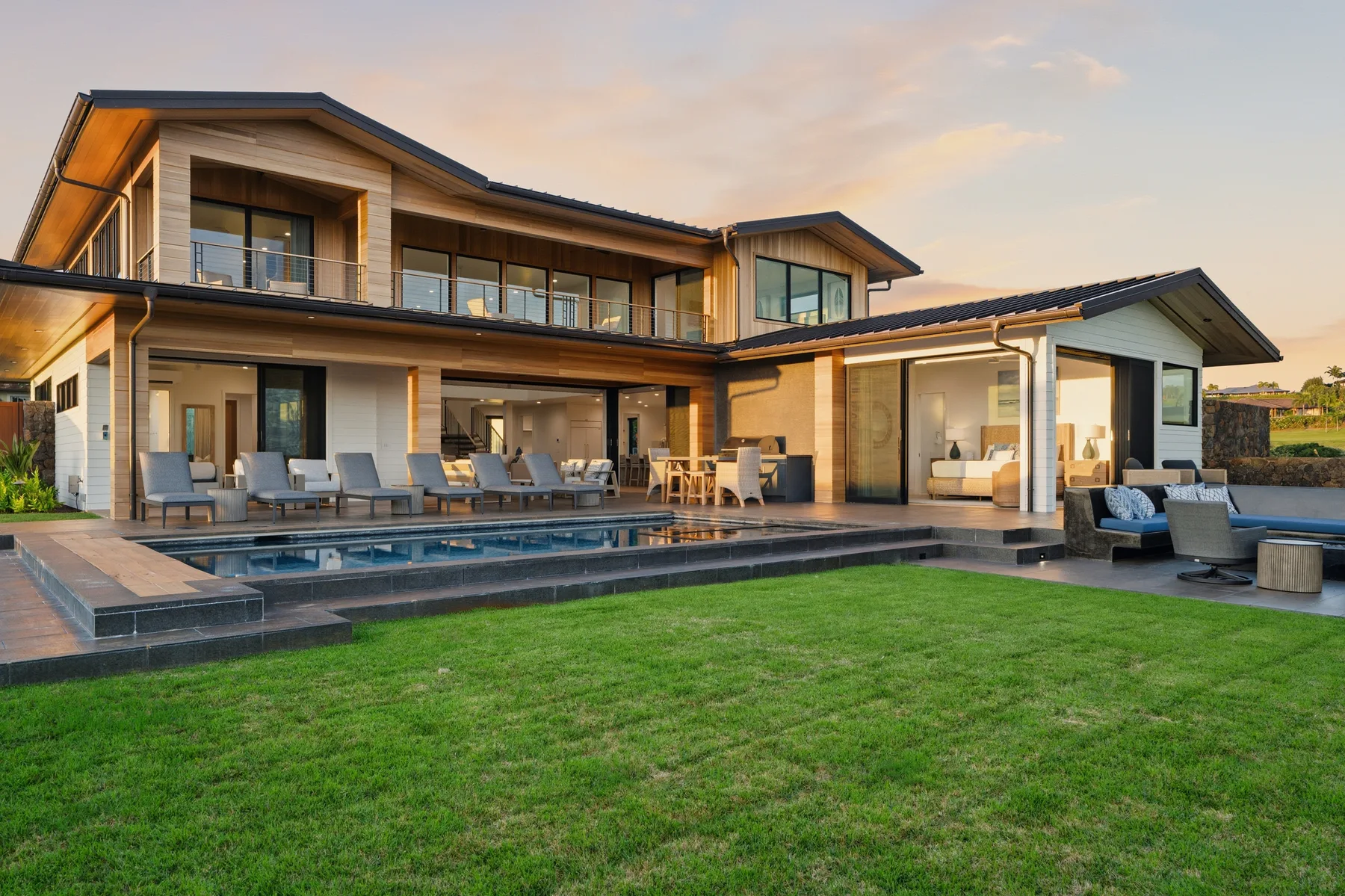 A modern house opens onto a swimming pool, patio seating, and a broad lawn.