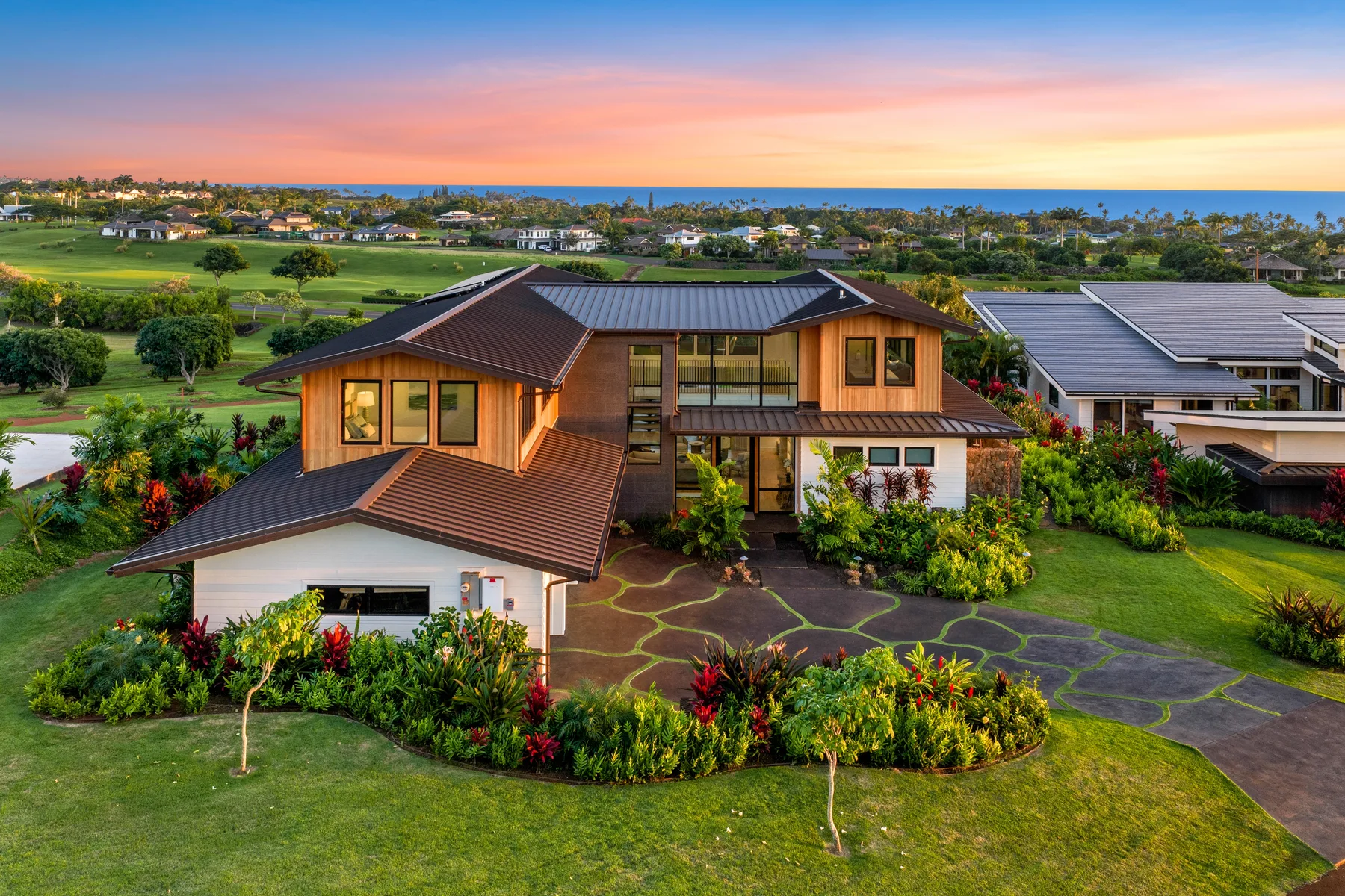 A modern house surrounded by landscaped gardens, with the ocean visible in the distance.