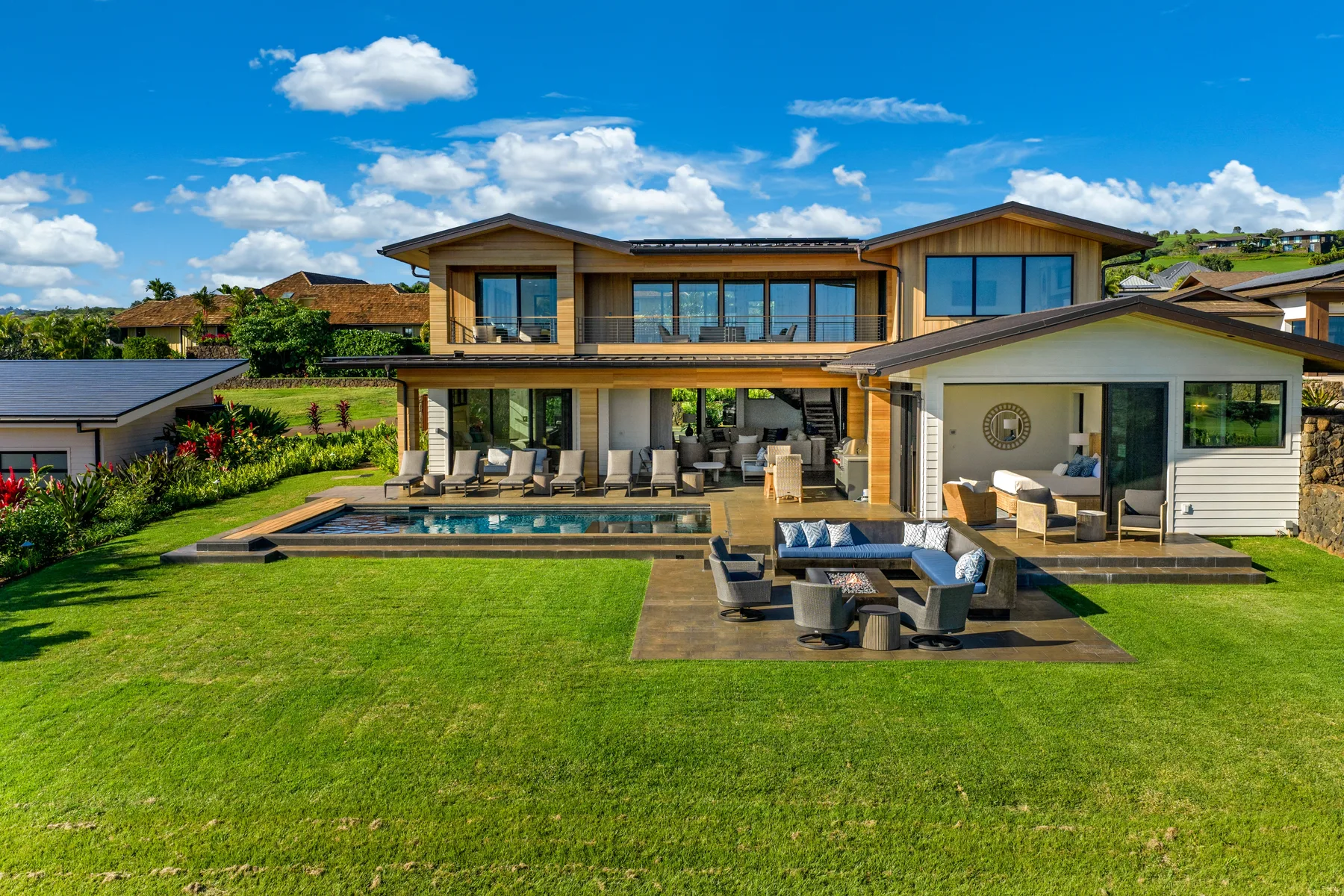A modern house opens onto a patio, swimming pool, and broad green lawn.