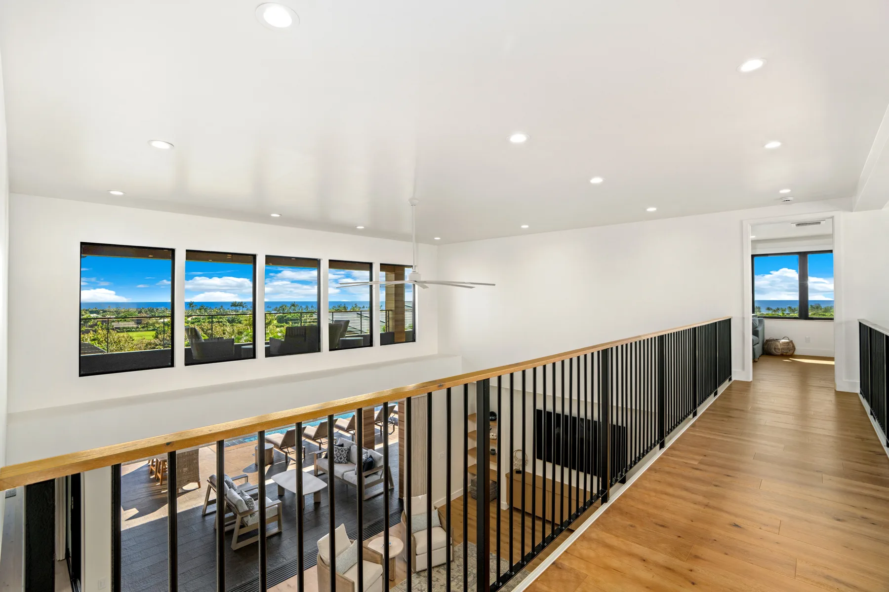 An upstairs landing with a wood floor and railing overlooking a dining area.