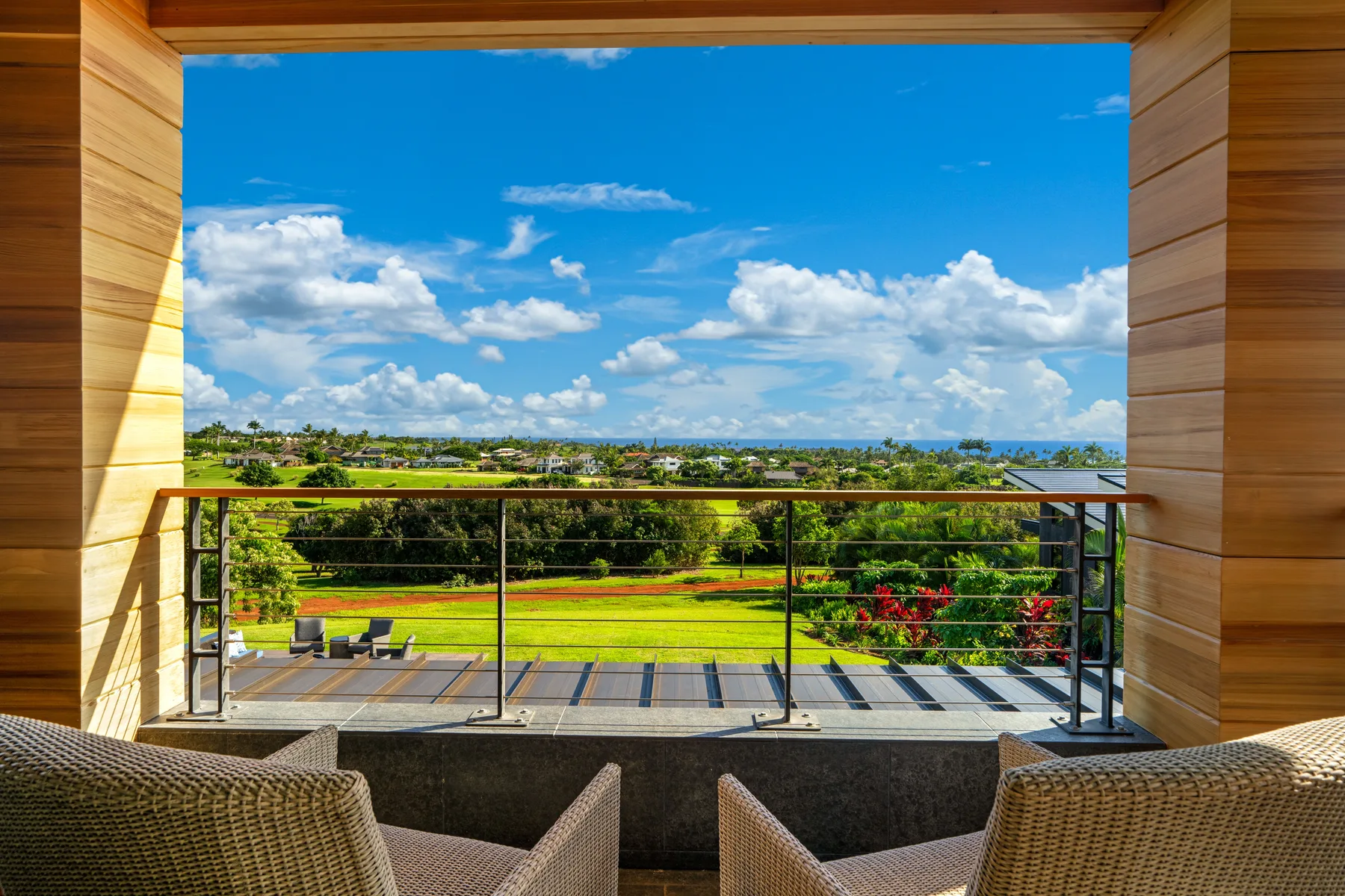 A balcony with woven seating overlooks a green landscape beneath a blue sky.