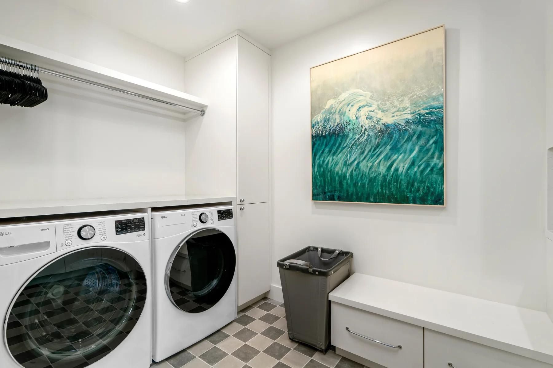 A laundry room with front-loading machines and a counter beneath ocean-wave artwork.