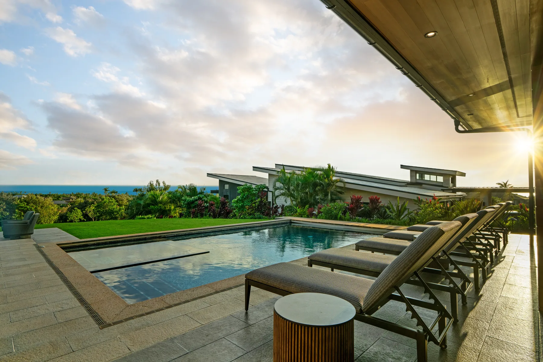 An outdoor pool beside lounge seating overlooks the sea at sunset.