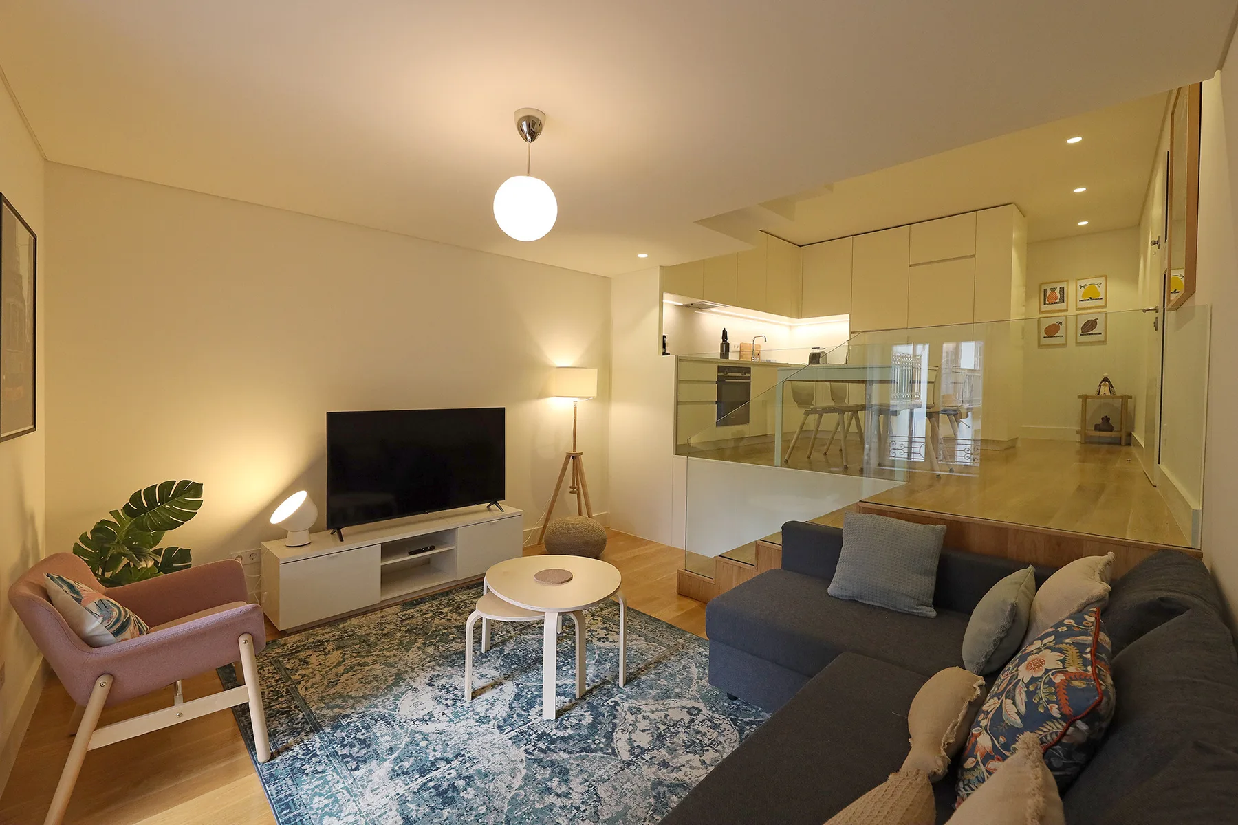 A living room with seating, a television, and a dining area beyond a glass partition.
