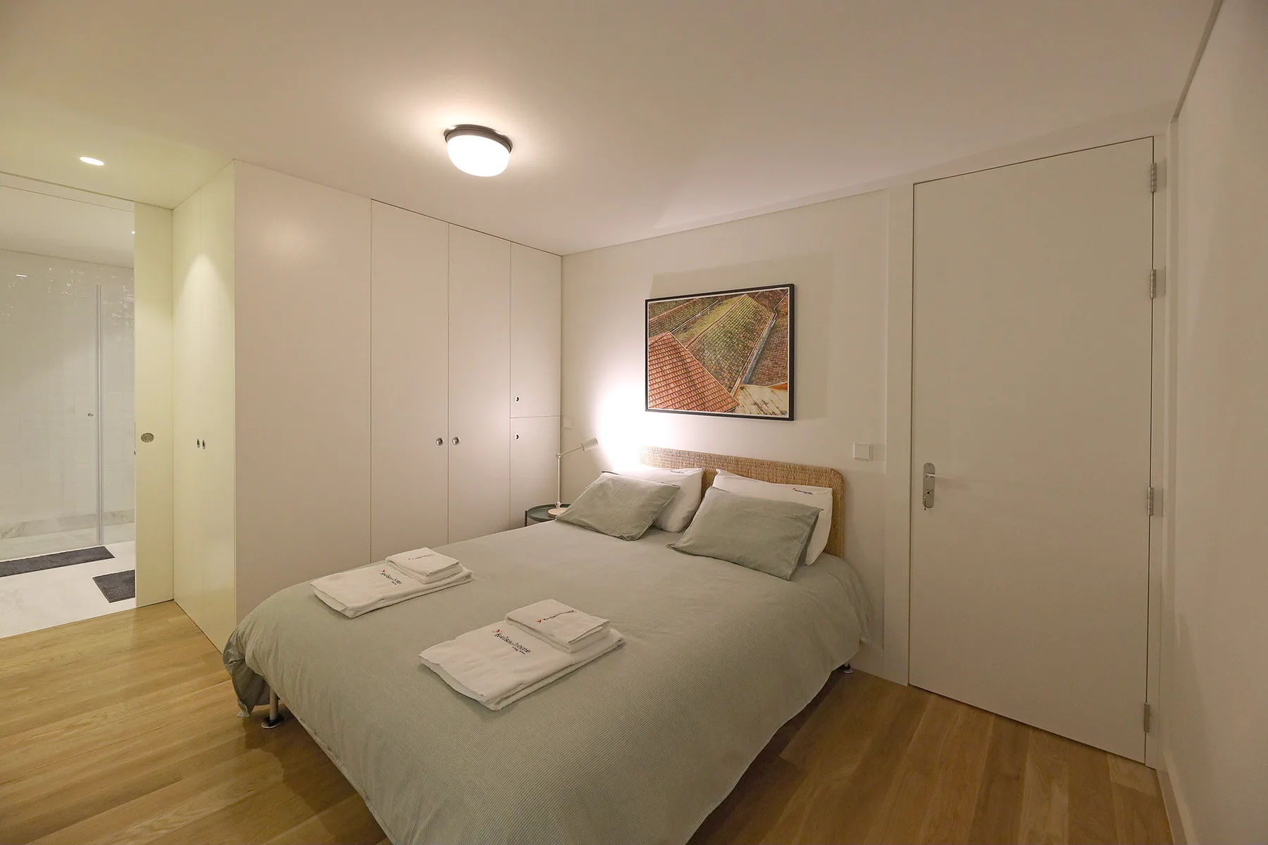 A bedroom with a neatly made bed, bedside tables, and built-in wardrobes.