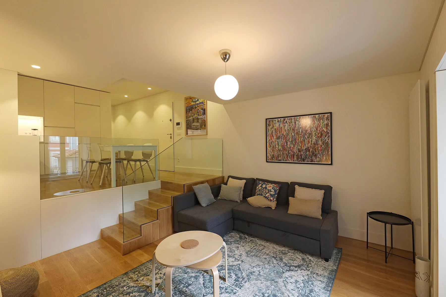 A living room with seating, a rug, and stairs beside a dining area.