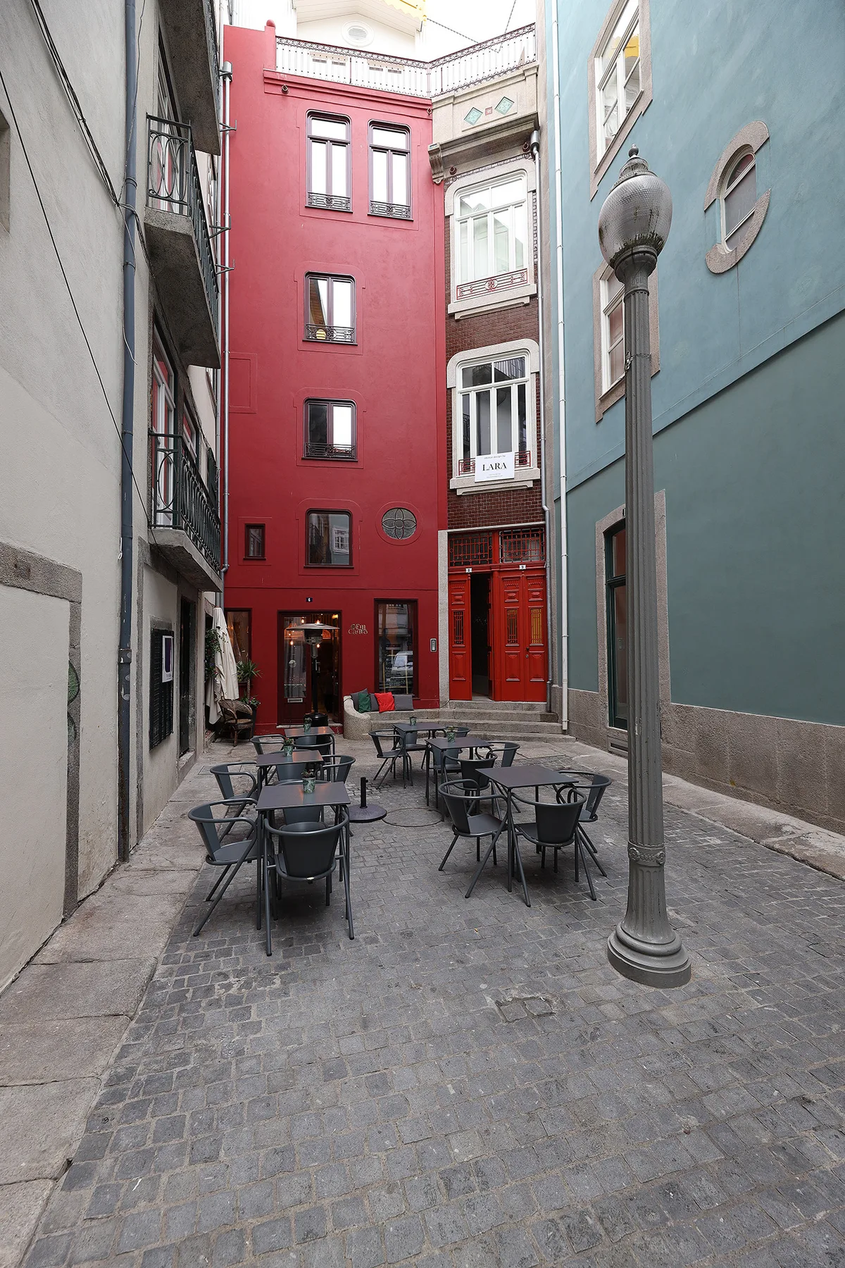 A narrow cobbled courtyard with outdoor tables between colorful multistory buildings.