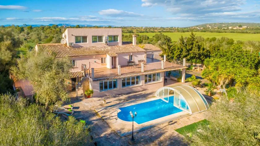 A large house overlooks a swimming pool and surrounding green countryside.
