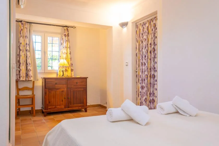 A bedroom with a wooden dresser, a window, and a bed with folded towels.