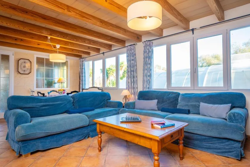 A living room with blue seating, a wooden coffee table, and large windows.
