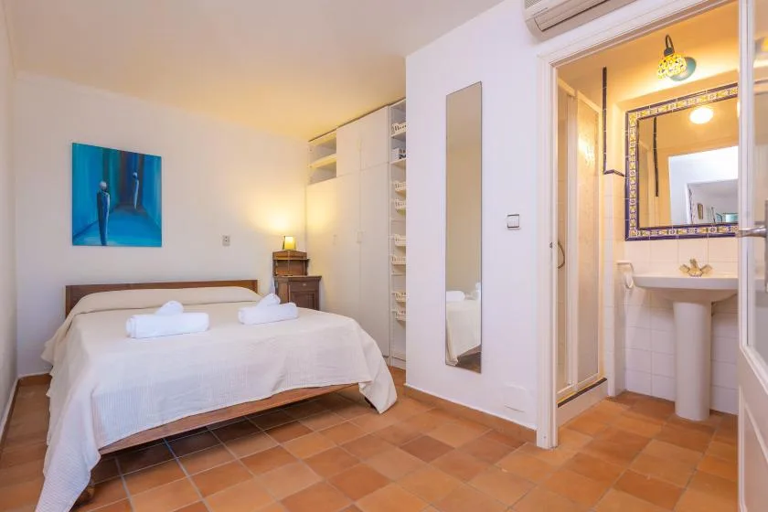 A bedroom with a neatly made bed beside an open bathroom area.