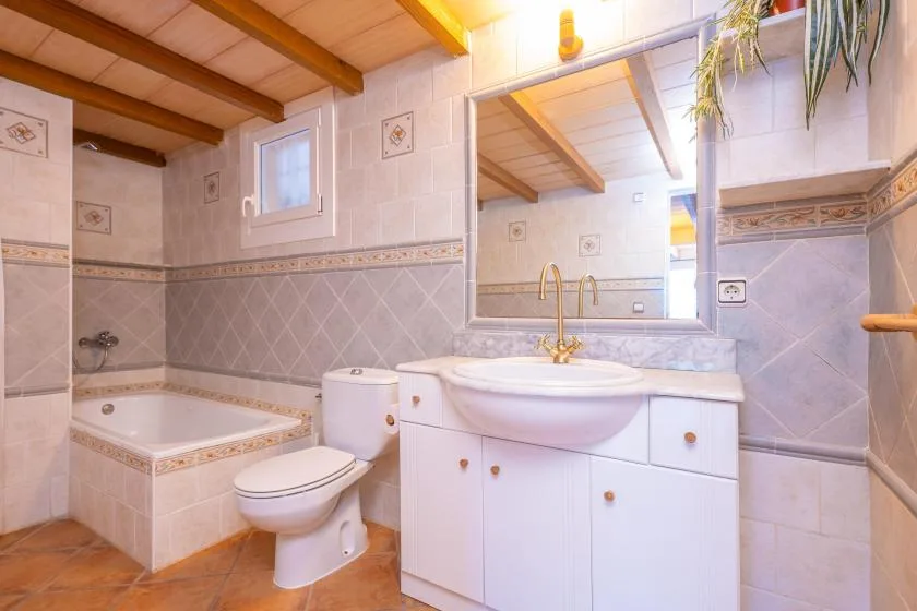A tiled bathroom with a bathtub, toilet, and sink beneath a large mirror.