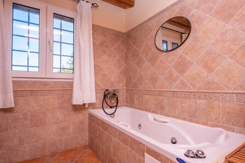 A tiled bathroom with a white bathtub beneath the windows.