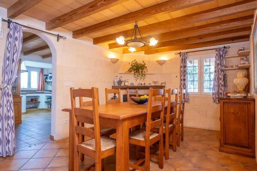 A dining room with a wooden table and chairs beneath exposed ceiling beams.