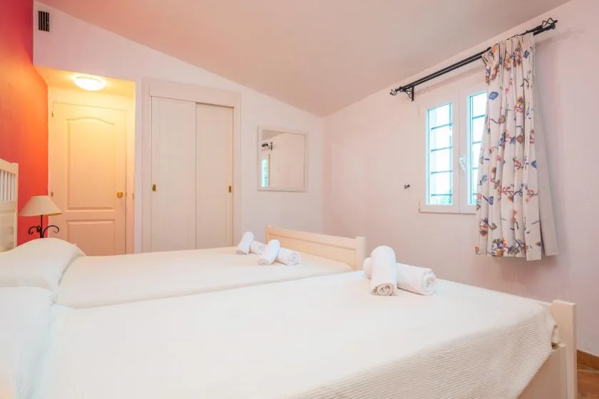 A bright bedroom with white beds and a curtained window.