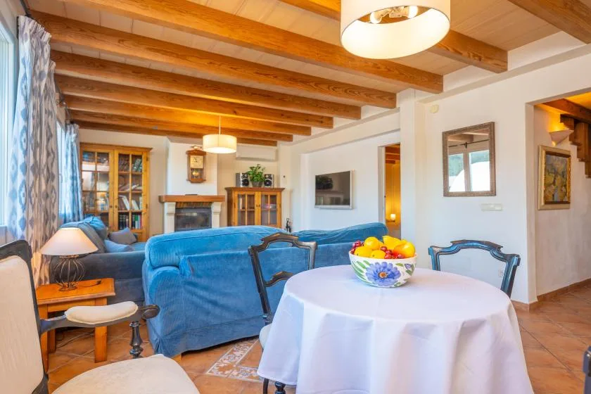 A living room with blue seating and a round dining table beneath exposed wooden beams.