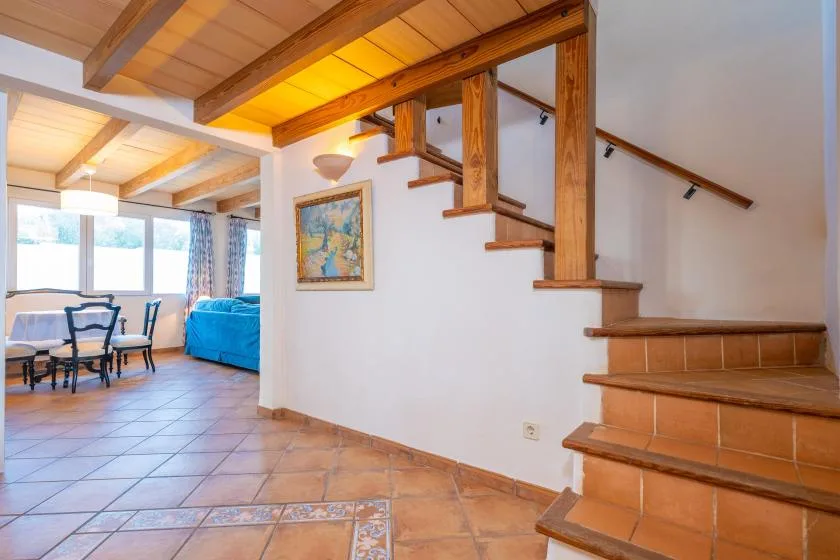 A tiled interior opens onto a dining area and a staircase beneath exposed wooden beams.