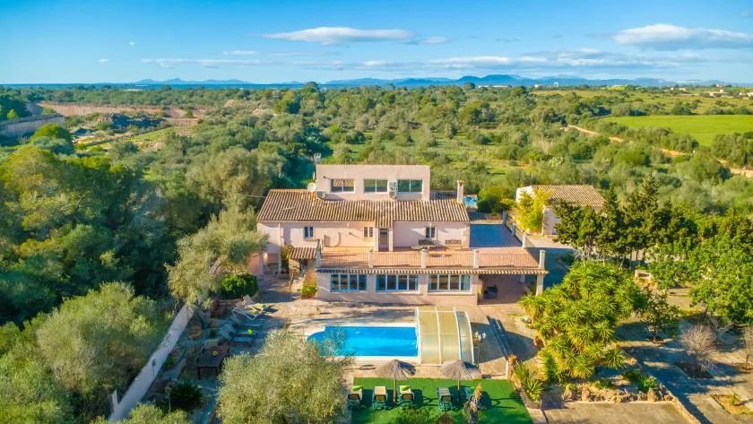 Aerial view of a country house with a swimming pool amid green countryside.