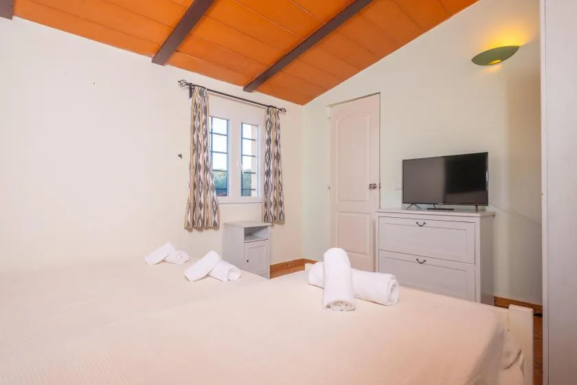 A bedroom with a bed, curtained window, and television on a dresser.
