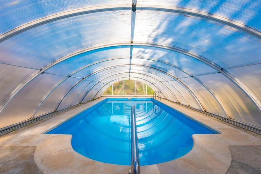 A swimming pool sits beneath a curved transparent canopy.