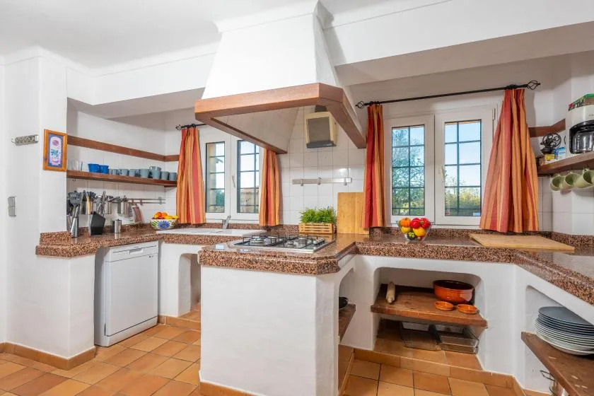 A bright kitchen with a central counter, cooktop, and windows.