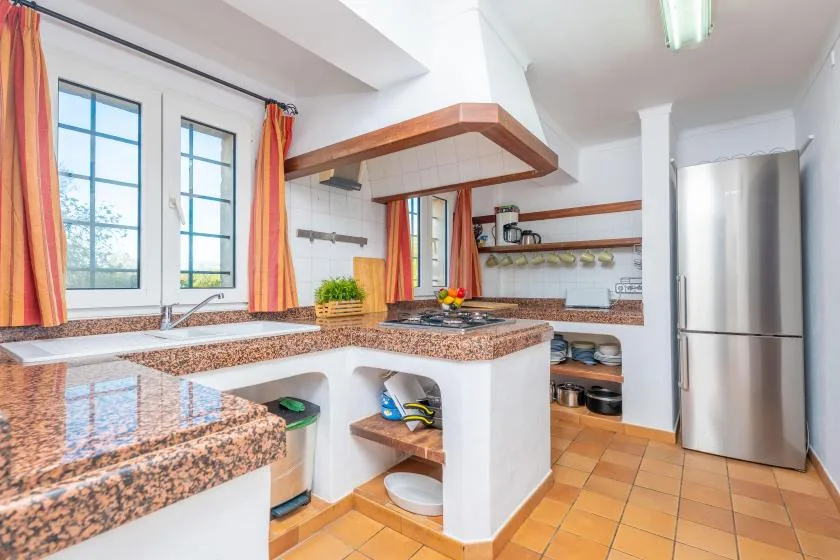 A kitchen with a granite countertop, cooking area, and stainless steel refrigerator.