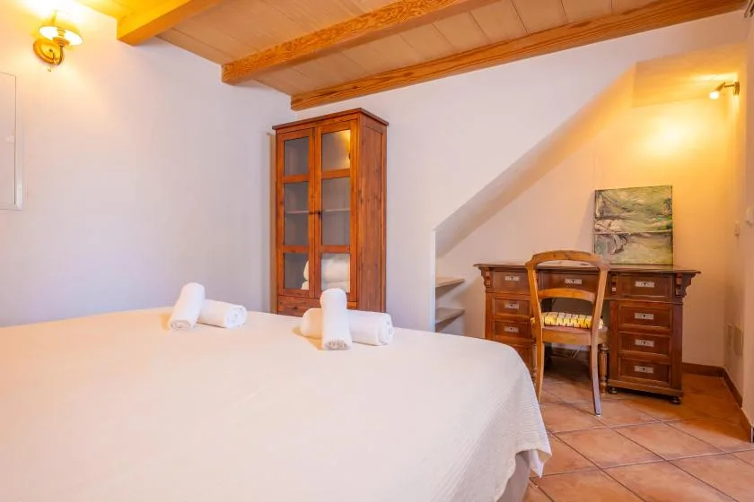 A bedroom with a large bed, wooden cabinet, and writing desk.