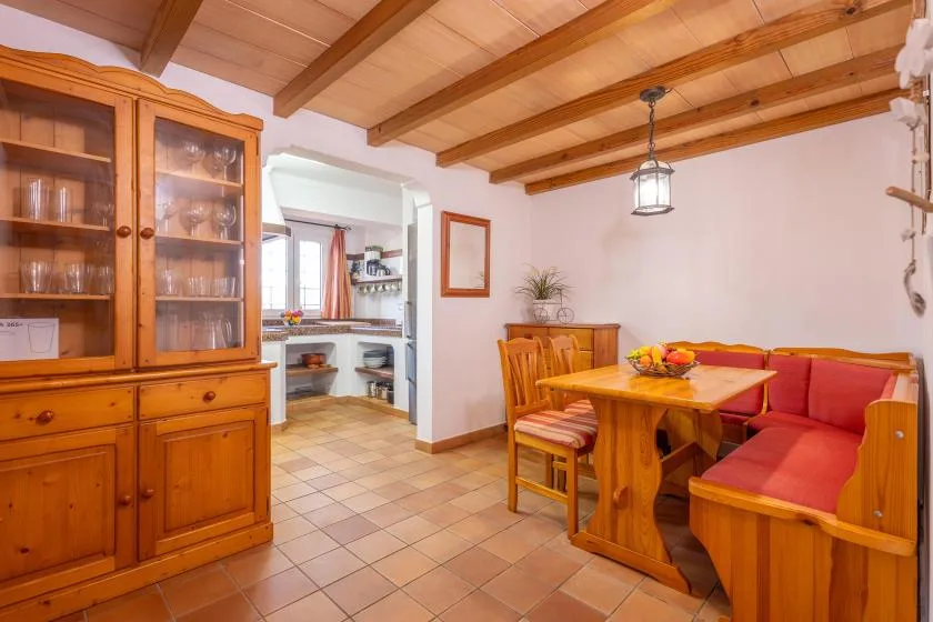 A dining area with wooden seating, a table, and a cabinet beneath exposed ceiling beams.