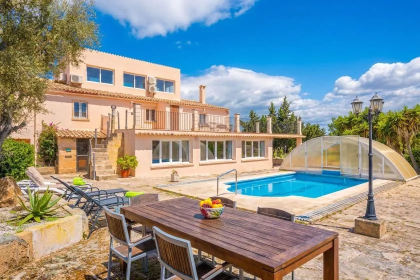 A swimming pool and outdoor dining area beside a large house.